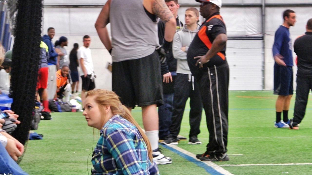 NFL coach on the sideline with players warming up behind.